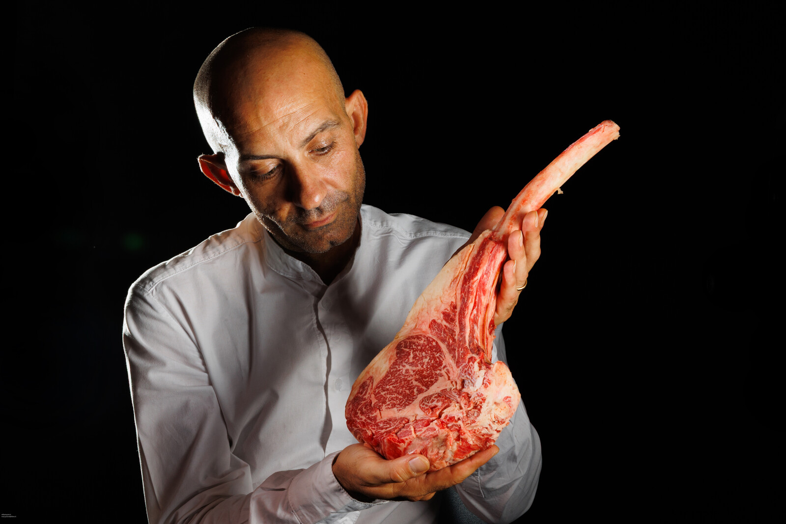 Il macellaio mostra un tomahawk crudo tenendolo per l osso
