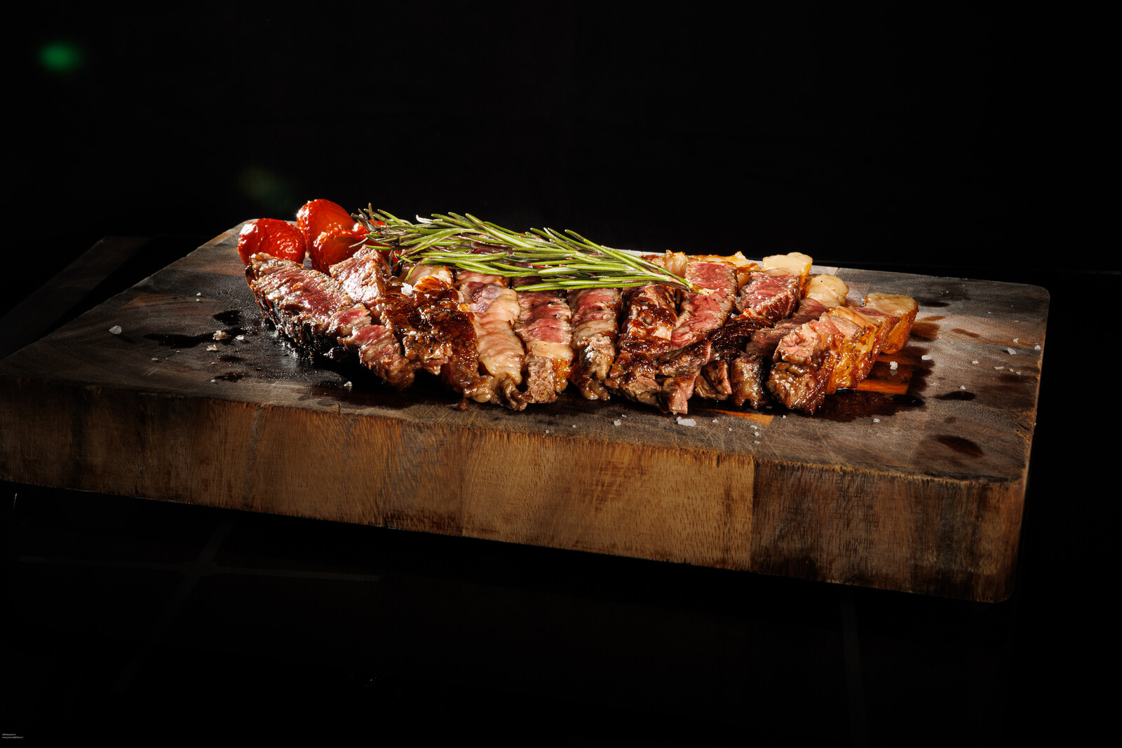 Carne alla brace affettata su tagliere di legno con rosmarino e pomodorini