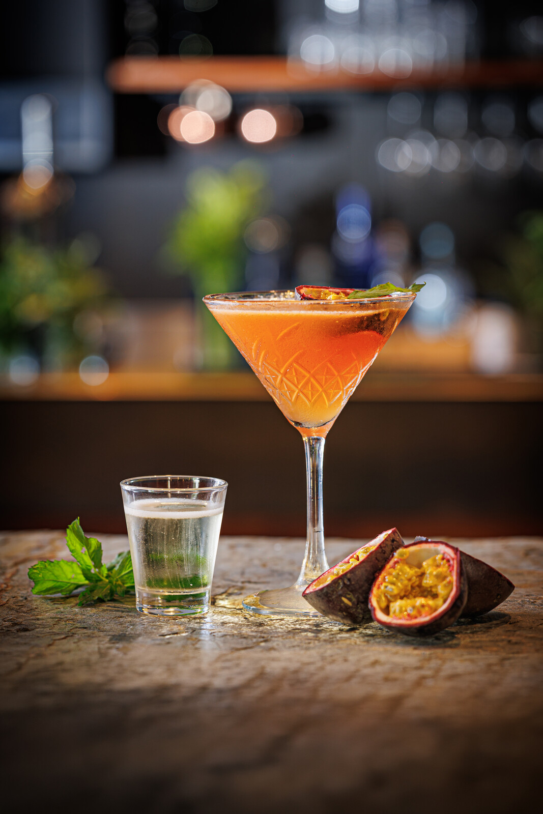 Cocktail arancione in coppa con frutto della passione e bicchierino a lato