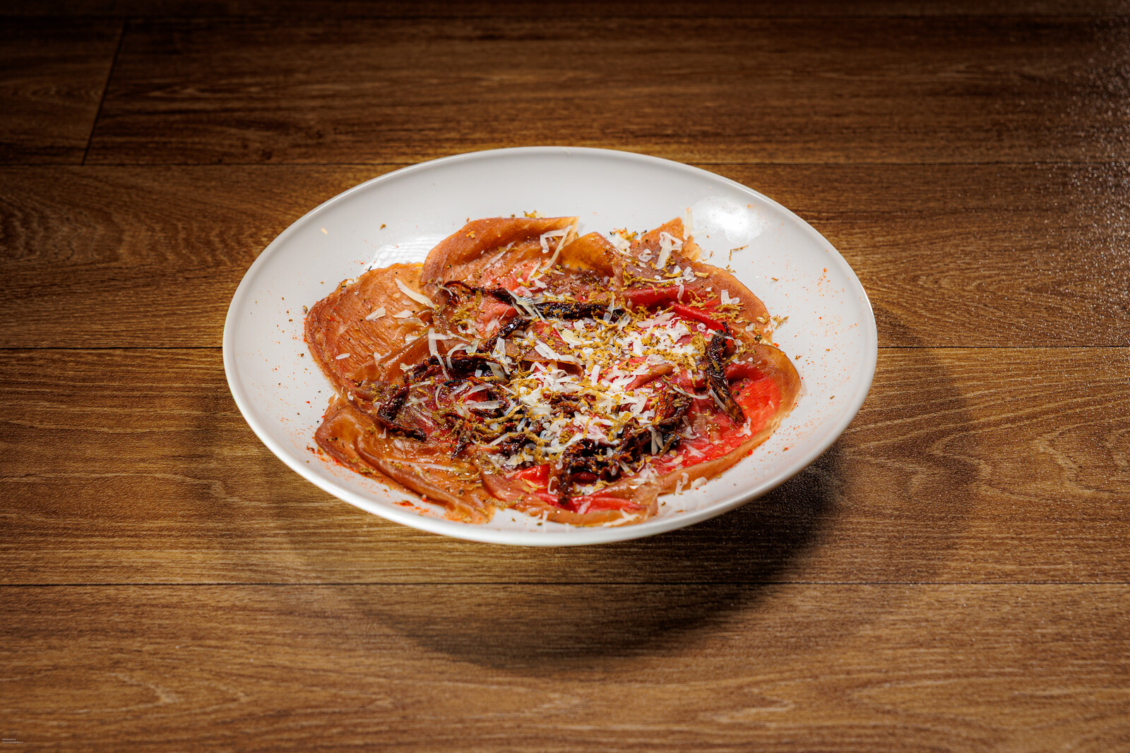 Carpaccio con scaglie di formaggio su piatto bianco
